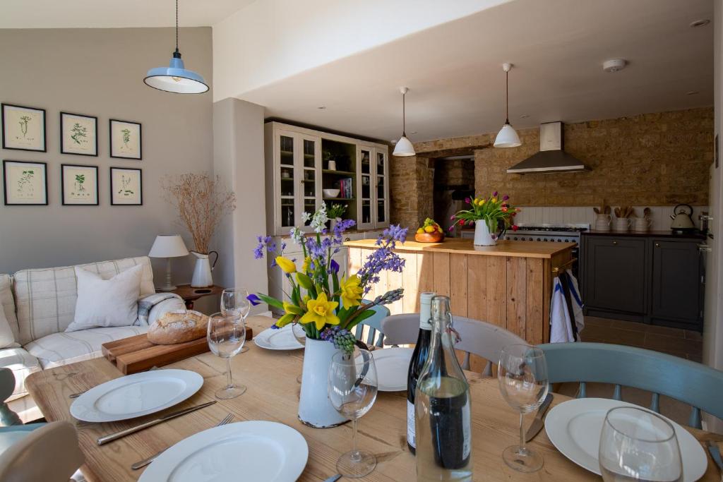 une salle à manger avec une table avec des fleurs et des verres à vin dans l'établissement Gleneda Cottage - a renovated, traditional Cotswold cottage full of charm with fireplace and garden, à Bourton on the Hill