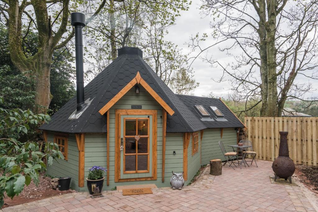 een klein huis met een zwart dak en een patio bij Punch Tree Cabins Couples Outdoor Bath in Carluke