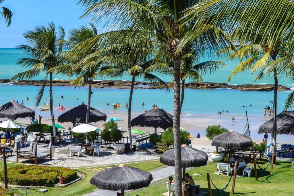 a beach with palm trees and people in the water at O paraíso em um flat à beira-mar de Carneiros in Tamandaré