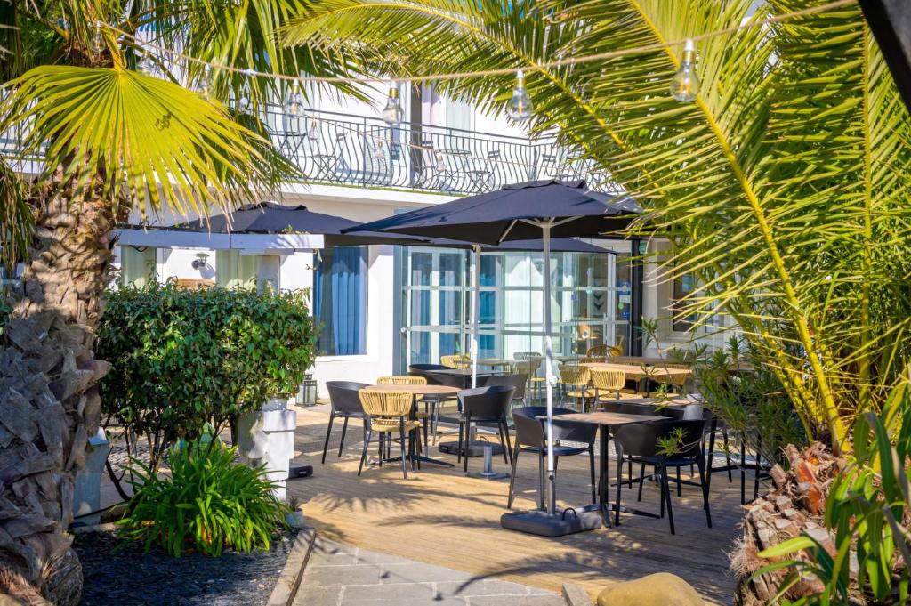 an outdoor patio with tables and chairs and umbrellas at Hôtel Le Martray in Ars-en-Ré