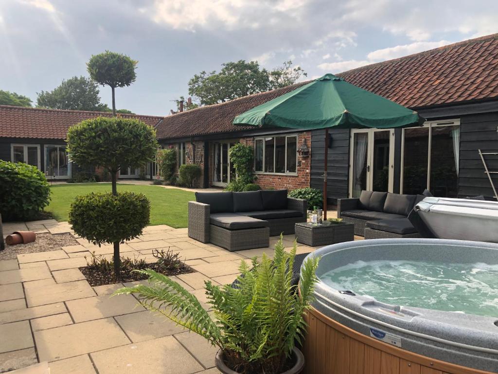 a patio with a hot tub and a green umbrella at WOW Lodge Farm Broads Barn sleeps 12 Hot tub Private Courtyard Special family celebrations Elegant dining Close to Norwich Great for Team Building in South Walsham