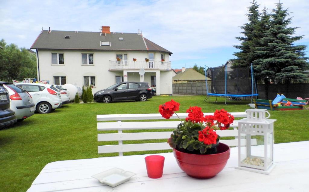 uma mesa branca com um vaso de flores vermelhas e uma casa em Pokoje Gościnne - U Wiktorii em Krynica Morska