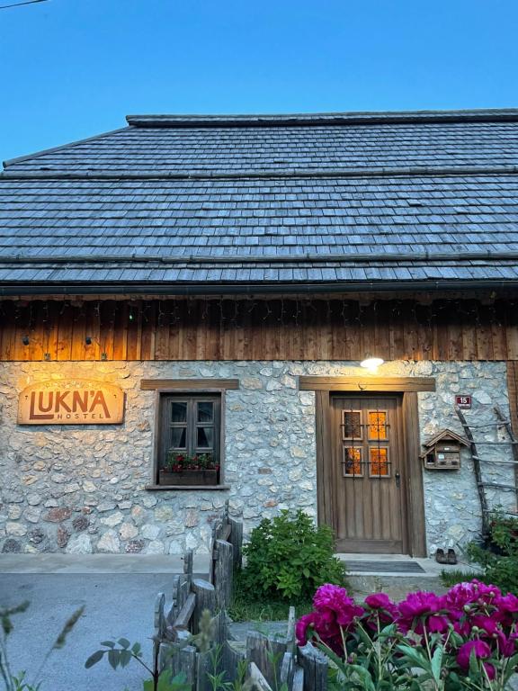 a stone building with a door and windows and flowers at Hostel Lukna in Mojstrana