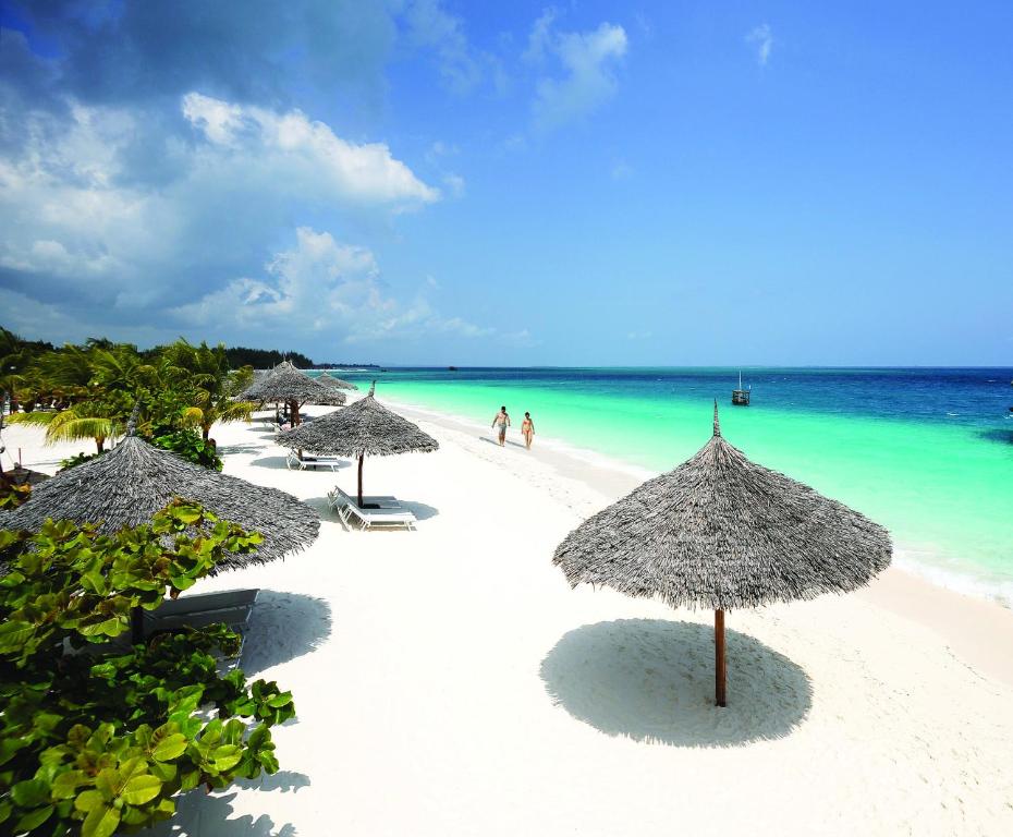 a beach with umbrellas and people in the water at Zanzibar Star Resort in Nungwi