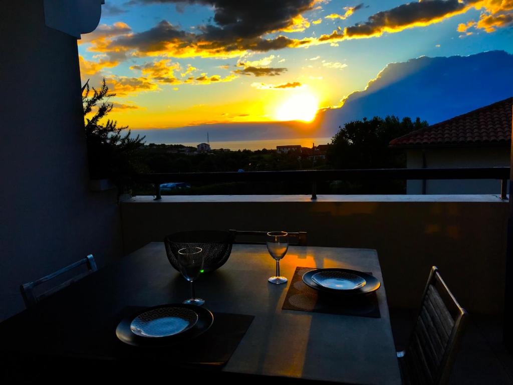 - une table avec deux verres sur un balcon avec vue sur le coucher du soleil dans l'établissement LE STUDIO D'ANTXETA Vue Océan, à 2 pas de Guethary, à Saint-Jean-de-Luz