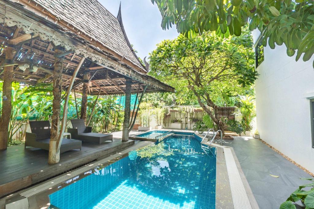 A bright pool borders a thatched lounging pavilion in a leafy courtyard.