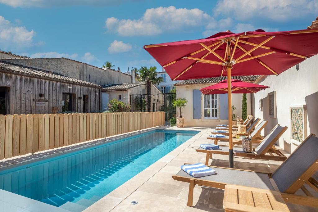 una piscina con sombrillas y sillas junto a una casa en La Baronnie Hôtel & Spa - Teritoria en Saint-Martin-de-Ré