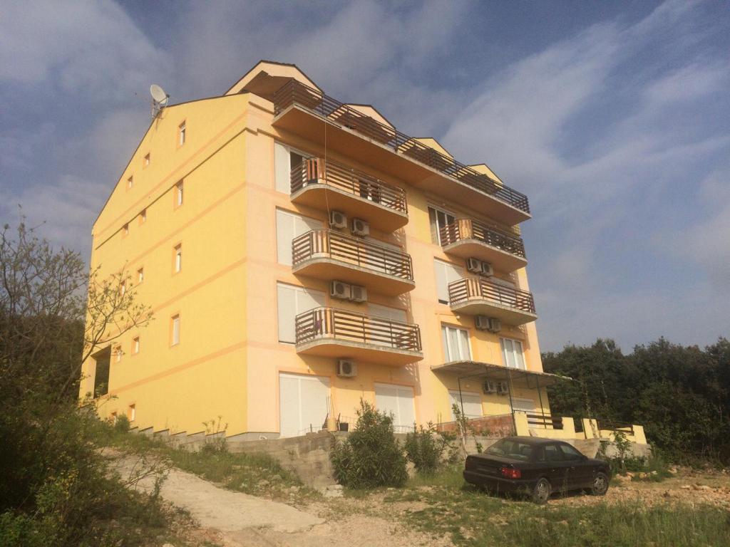 un edificio giallo con un'auto parcheggiata di fronte di Apartmani Vukovic a Tivat