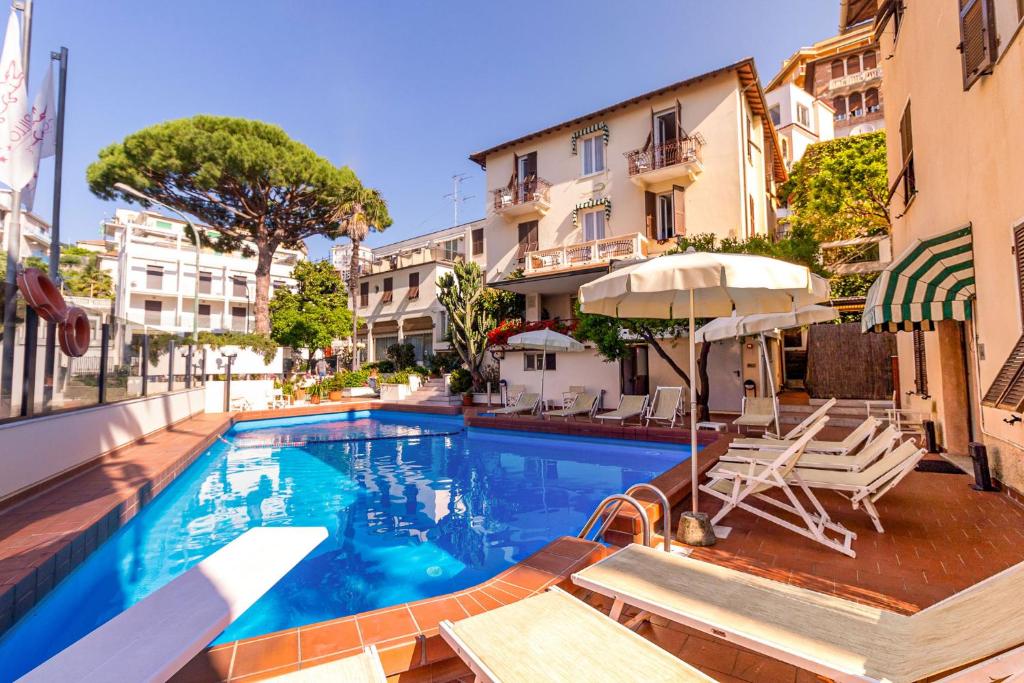 a swimming pool with chairs and an umbrella next to buildings at Coccodrillo Hotel & Apartments in Varazze