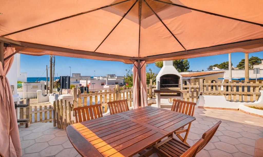 drewniany stół i krzesła z parasolem na patio w obiekcie Dimora Giusy Vista Mare Pescoluse w mieście Marina di Pescoluse