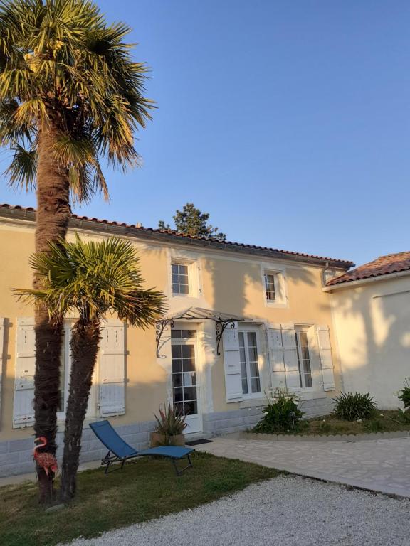 une maison blanche avec des palmiers et un banc bleu dans l'établissement A LA PAILLOTTE, à Brizambourg