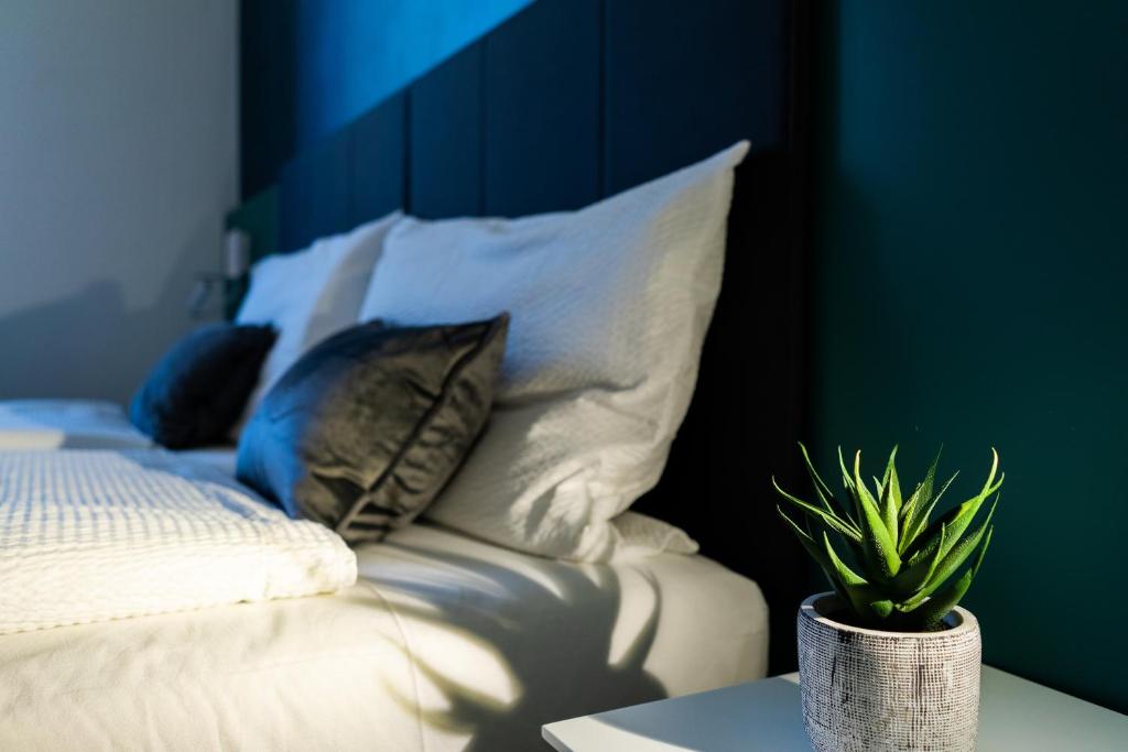 Una cama con almohadas blancas y una planta sobre una mesa en Appartamenti Vasco Renna Surf Center, en Nago-Torbole