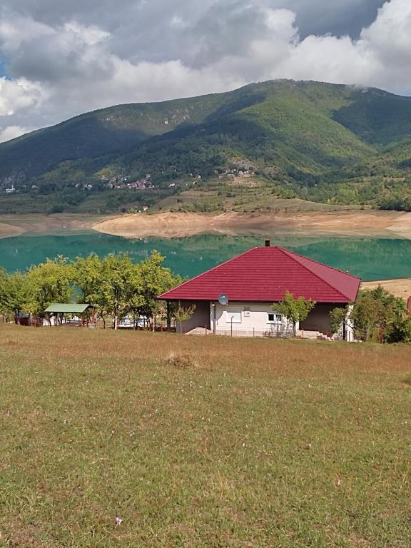 een huis met een rood dak voor een meer bij Bosnian Hobbiton in Kovačevo Polje