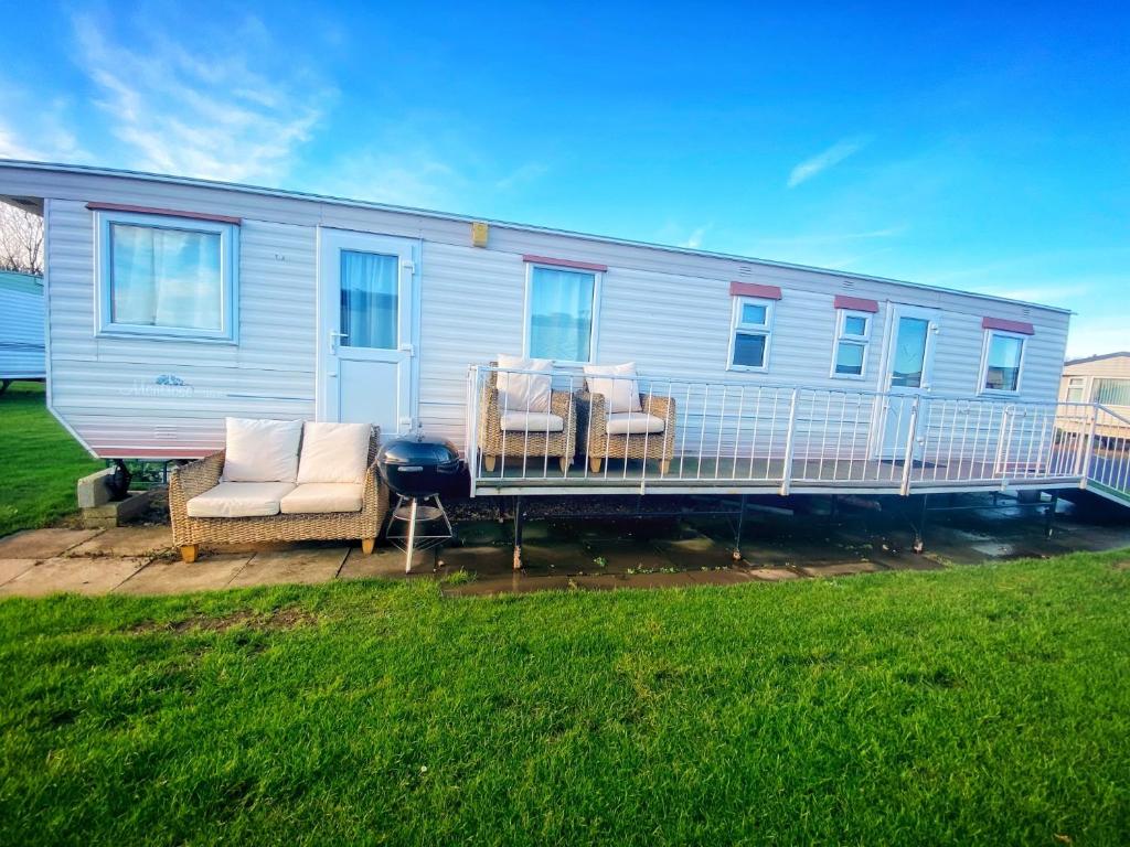 a mobile home with a deck with chairs and a grill at Family 5 beds static caravan in Lincolnshire