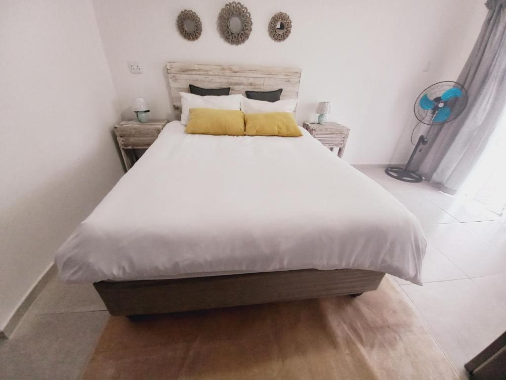 Una cama con sábanas blancas y almohadas amarillas en un dormitorio en Lime Court Three en Pretoria