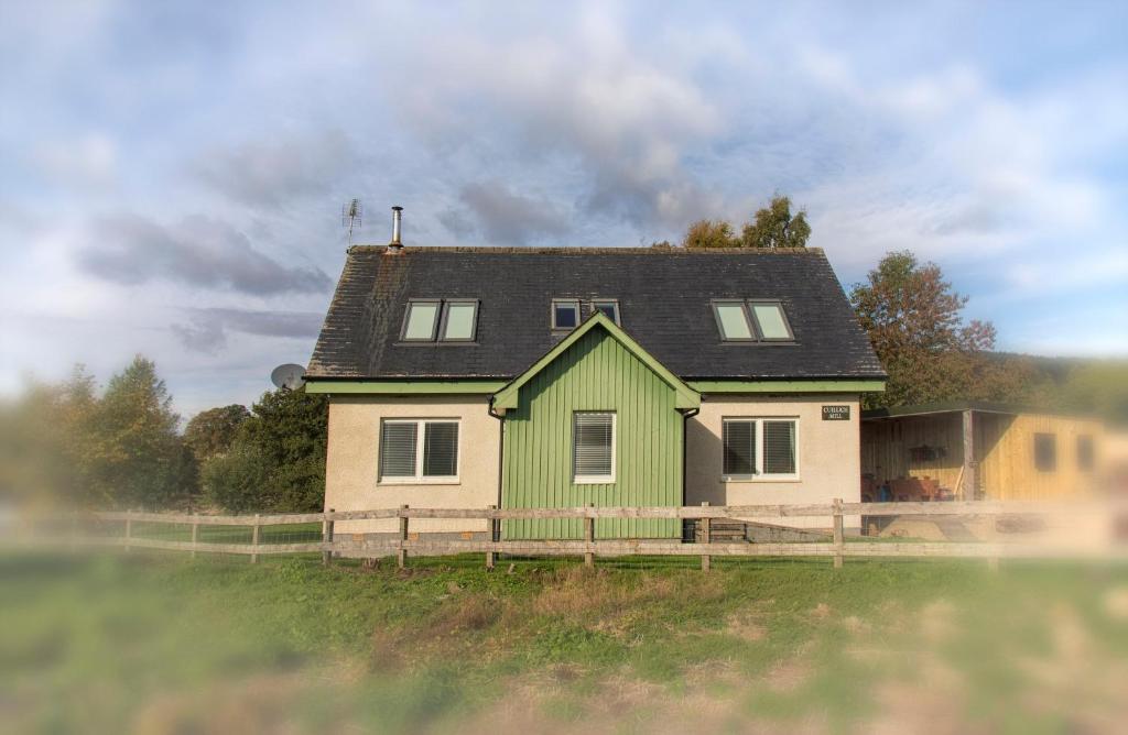 a green and white house with a wooden fence at Cuillich Mill Bed and Breakfast in the Highlands in Alness