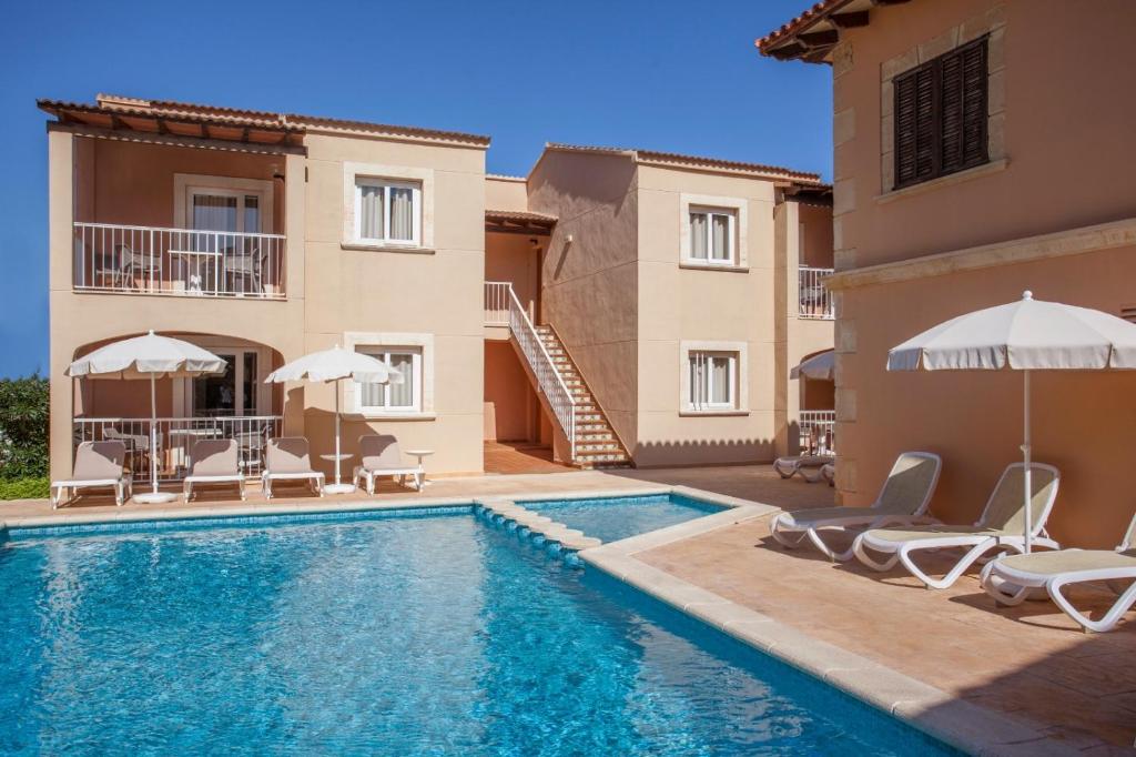 a pool with chairs and umbrellas next to a building at Agulla park in Cala Ratjada