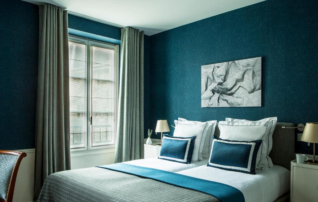 a bedroom with a bed with blue walls and a window at Hôtel de la Place du Louvre - Esprit de France in Paris