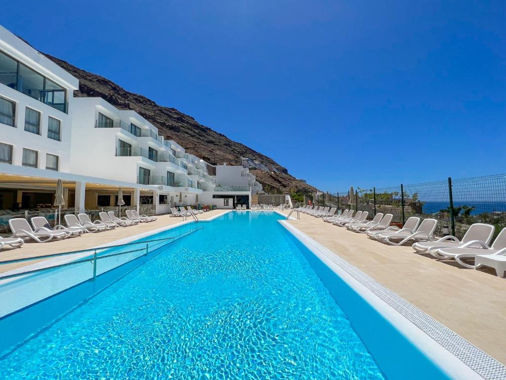 una piscina con sillas y un hotel en Apartamentos Cordial Magec Taurito, en Taurito