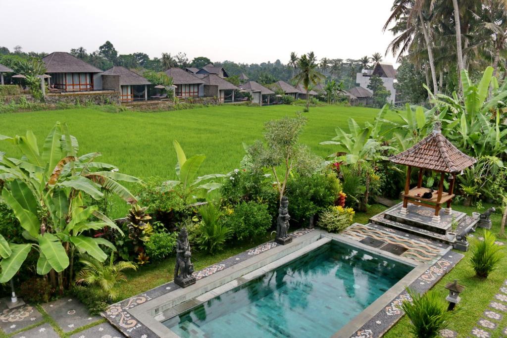 a swimming pool in a garden with a gazebo at Mira Family Cottages in Ubud