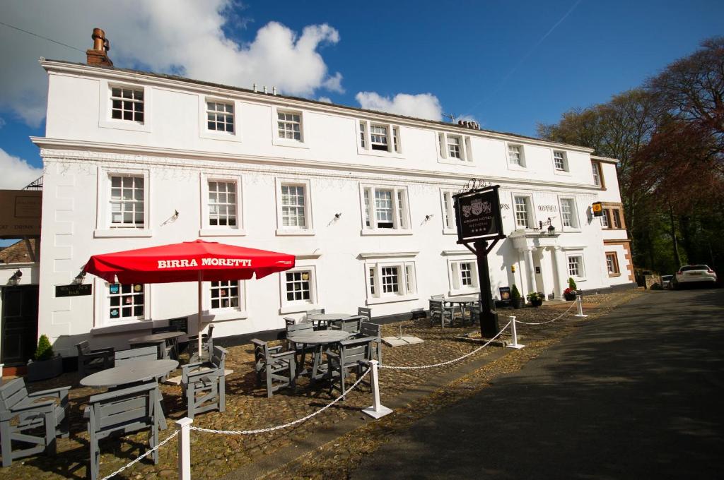 een wit gebouw met tafels en een rode paraplu bij Crown Hotel Wetheral in Carlisle