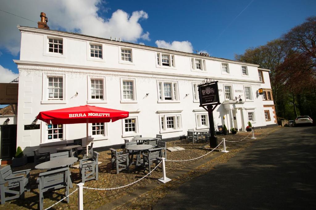 a white building with tables and a red umbrella at Crown Hotel Wetheral in Carlisle