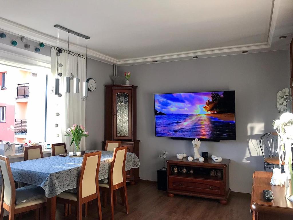 a dining room with a table and a television on a wall at Apartament SŁONECZNY Mrzeżyno in Mrzeżyno