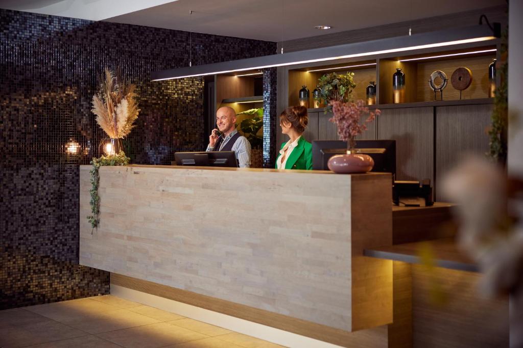 two people standing at a counter in a restaurant at Van der Valk Hotel Dennenhof in Brasschaat