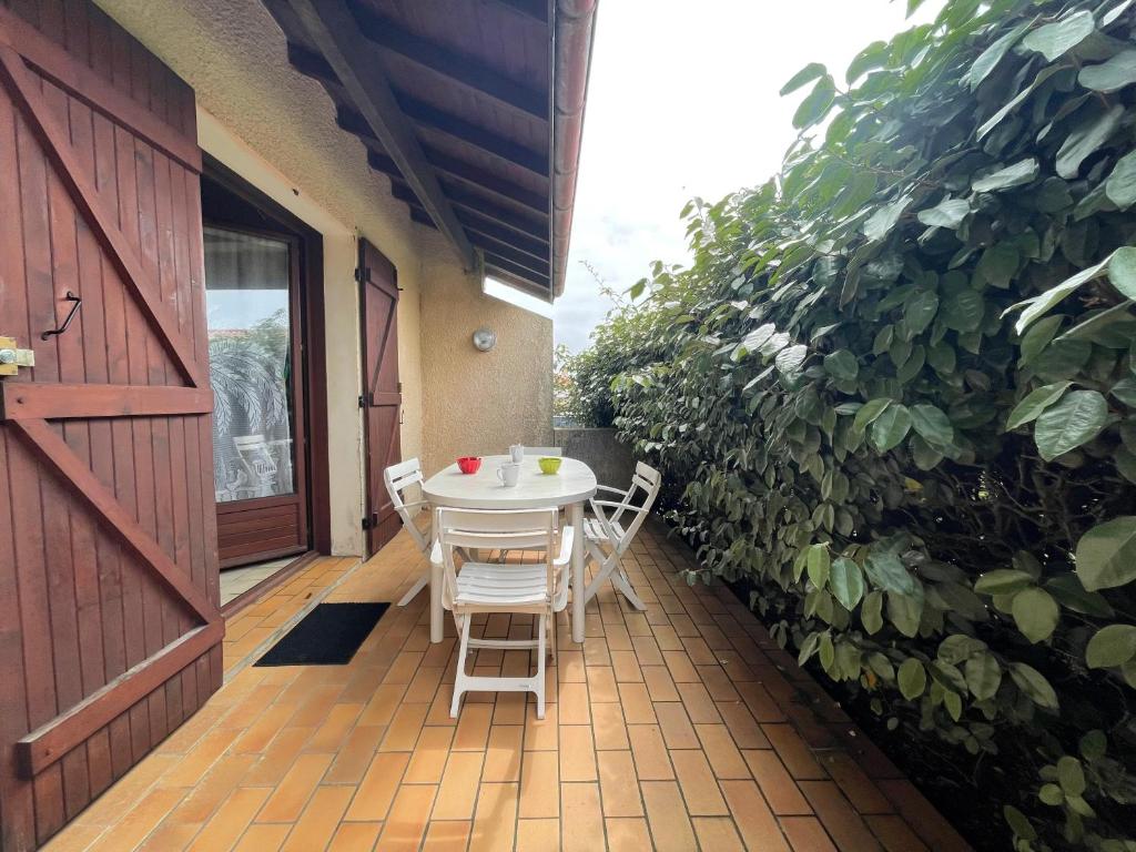 une table et des chaises sur une terrasse avec une haie dans l'établissement Les Pignes, à Mimizan
