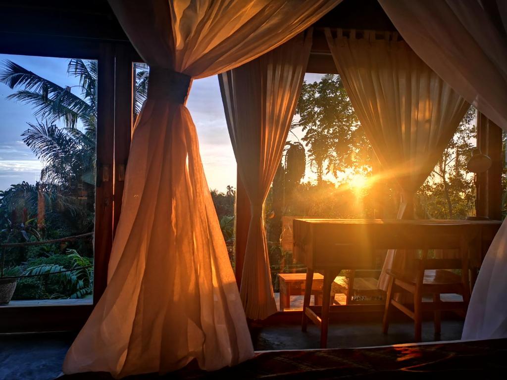 Cette chambre dispose d'une table et d'une fenêtre offrant une vue sur le coucher du soleil. dans l'établissement Villa Rimba Ubud, à Tegalalang