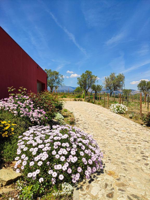 a dirt road with flowers next to a red building at Quinta dos Padrinhos - Suites in the Heart of the Douro in Lamego