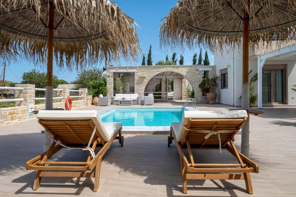 a villa with a swimming pool with two chairs and umbrellas at Golden Sky Villa in Kamilari