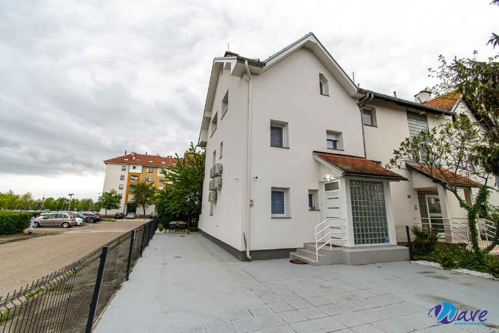 a white house with a fence next to a street at MODERN apartments WAVE near the AIRPORT in Velika Gorica