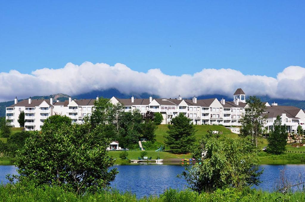 a large apartment building with a lake in front of it at Manoir des Sables Hôtel & Golf in Magog-Orford
