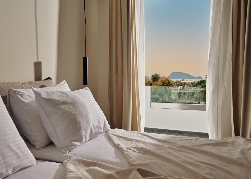 a bed with white sheets and pillows in front of a window at Amaroo Suites in Laganas