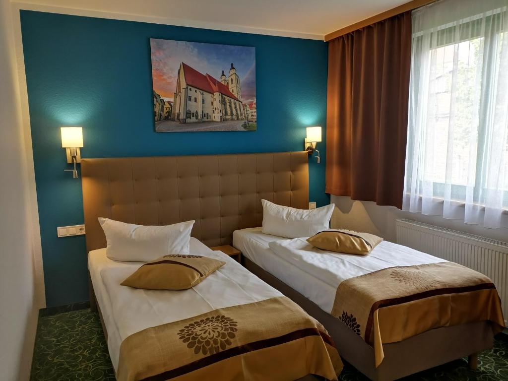 two beds in a hotel room with blue walls at ACRON Hotel Wittenberg in Lutherstadt Wittenberg