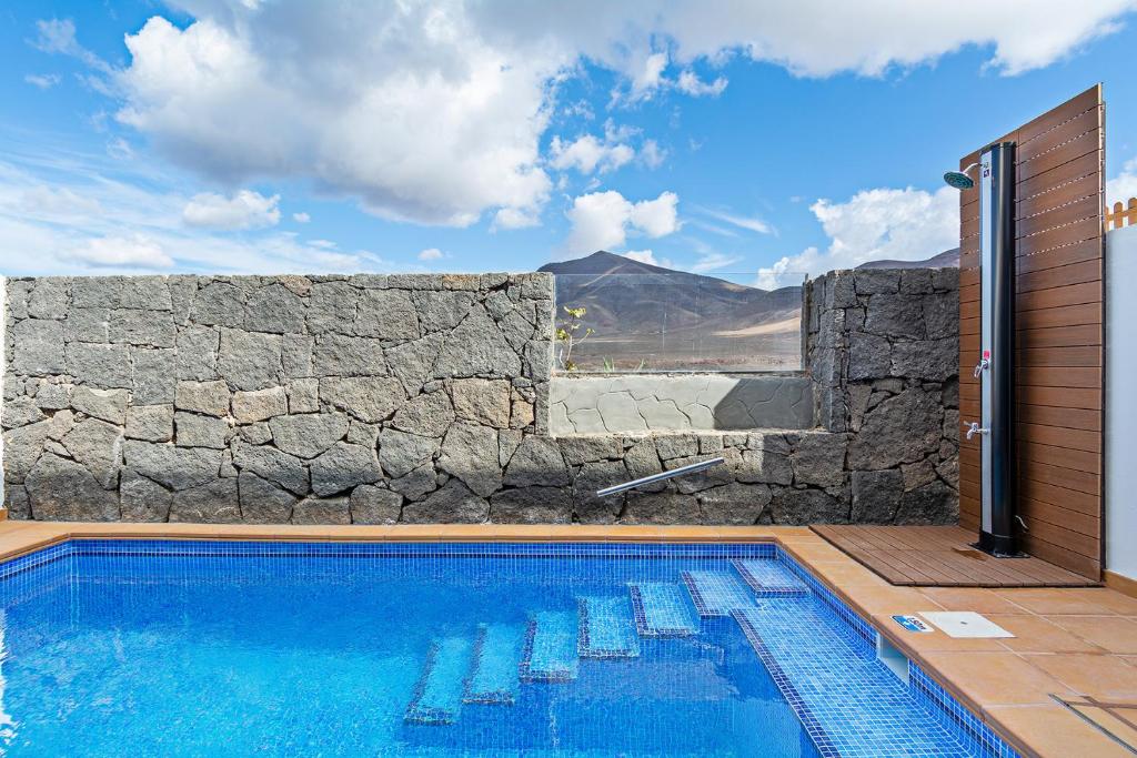 une piscine avec des chaises et un mur en pierre dans l'établissement 3BR Home - Private Heated Pool - Parking, à Playa Blanca