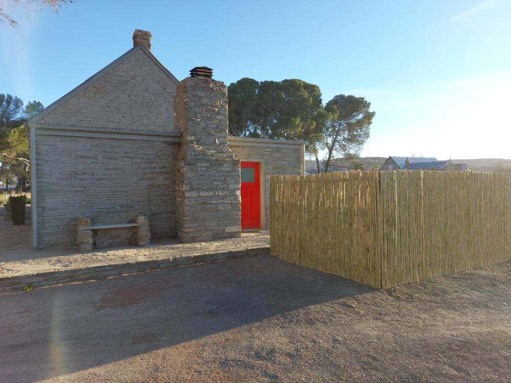 a building with a red door next to a fence at Little Artist Cottage in Sutherland