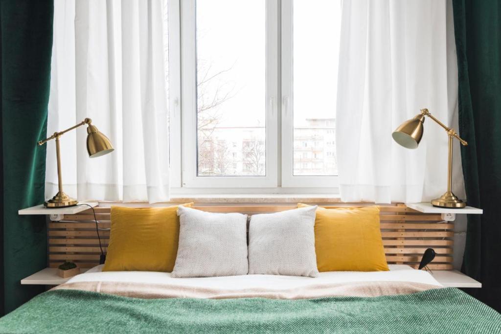 a bed with yellow and white pillows in front of a window at Lux Apartment II in Gdańsk
