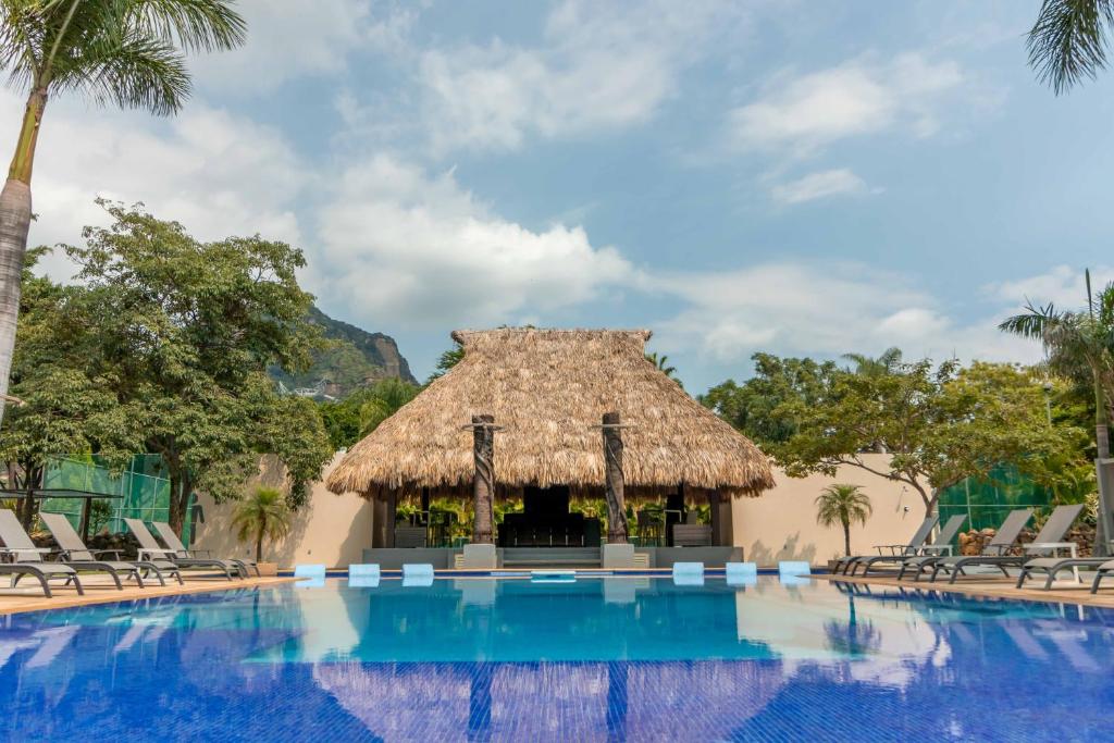 a pool at a resort with chairs and a thatch hut at Alilo by Muuk in Tepoztlán