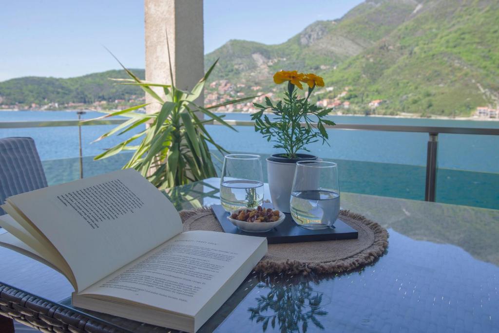 un libro aperto seduto su un tavolo con una ciotola di cibo e bicchieri di Apartments MaXhit a Tivat