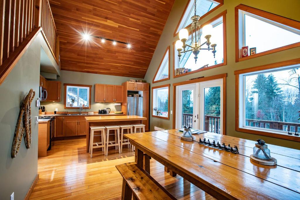 a large kitchen with a wooden table and some windows at Stoke Cabin by Revelstoke Vacations in Revelstoke