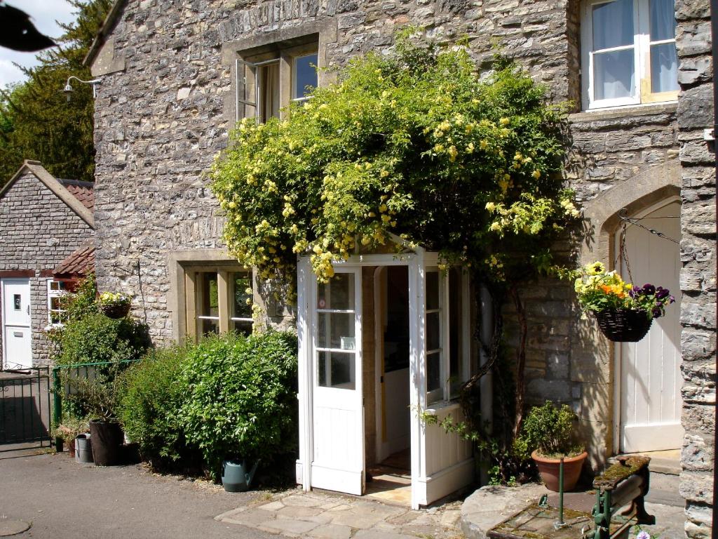 a stone house with a white door and flowers at Burcott Mill Guesthouse in Wells