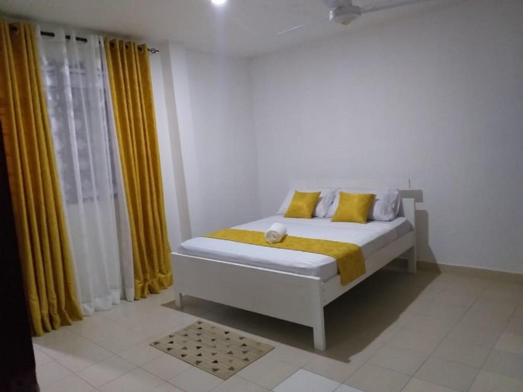 a white bedroom with a bed with yellow curtains at Hyven's Apartments in Mtwapa