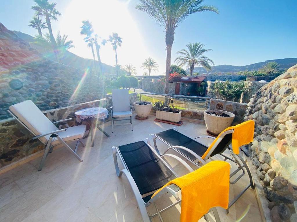 a patio with chairs and a table and palm trees at Fantastic Anfi Tauro Duplex with ocean view in Las Palmas de Gran Canaria