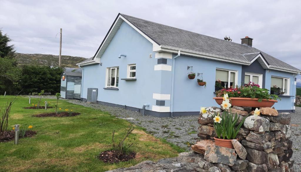 a blue house with a stone wall in front of it at Clifden Wildflower Cottage - Clifden Countryside Lettings in Clifden