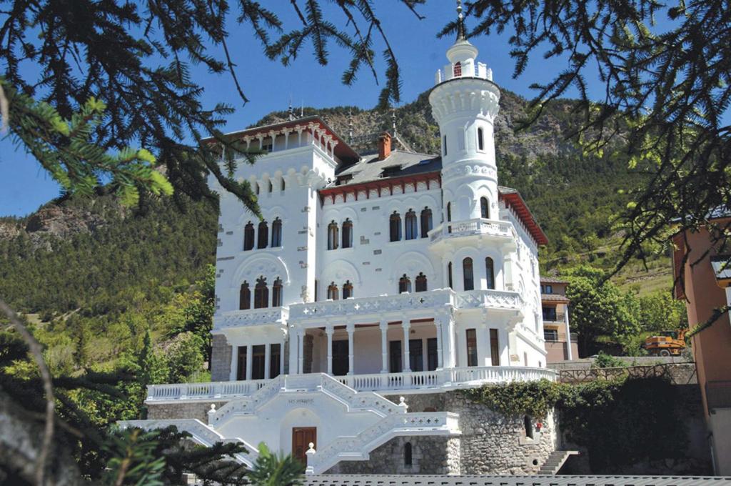 un bâtiment blanc avec une tour au sommet d'une montagne dans l'établissement Résidence Château des Magnans by Nevesol, à Jausiers