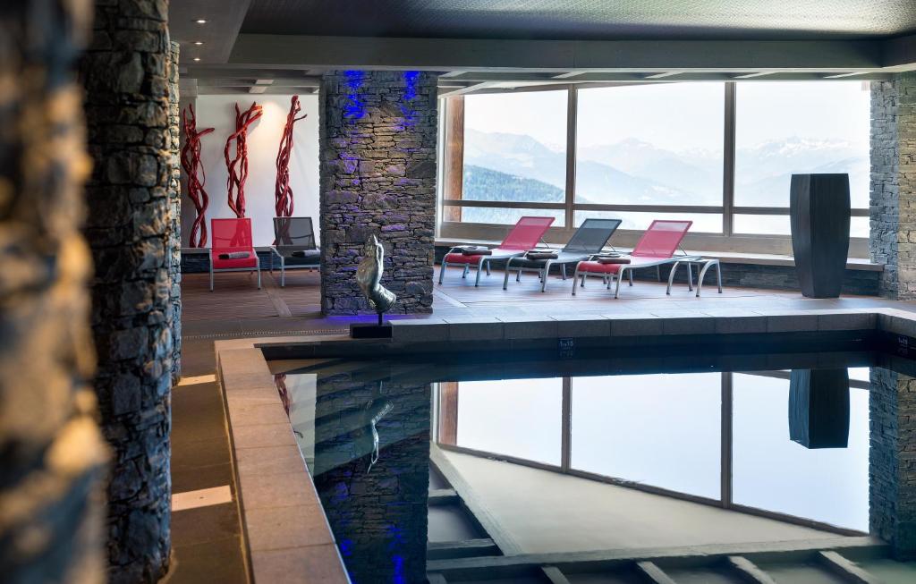 - une piscine dans un bâtiment avec des tables et des chaises roses dans l'établissement CGH Résidences & Spas Le Lodge Hemera, à La Rosière