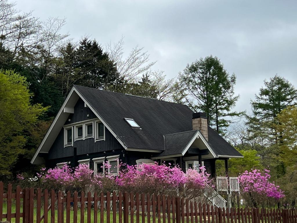 una casa nera con fiori rosa di fronte a una recinzione di 山中湖湖畔高級ログハウス 充電富士168 a Yamanakako