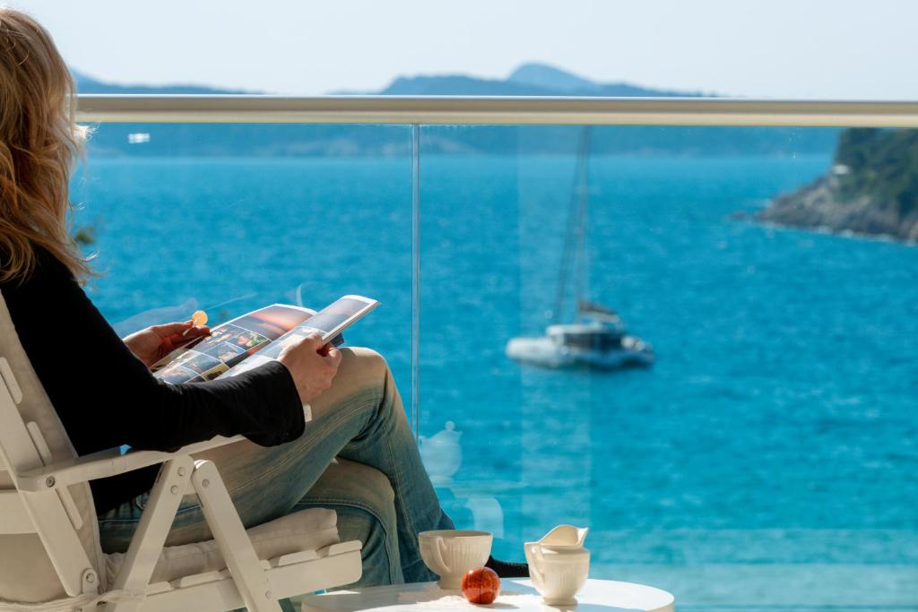 Eine Frau, die auf einem Stuhl sitzt und ein Buch liest und aus dem Fenster schaut. in der Unterkunft Apartments Dvori Lapad 2 Direct Sea View in Dubrovnik